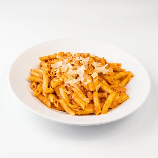 Penne pasta in a creamy tomato sauce, topped with shaved Parmesan cheese, on a white plate.