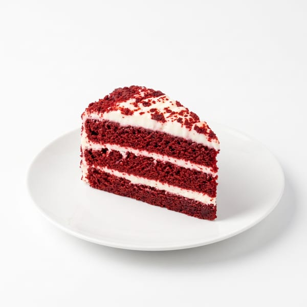 A slice of red velvet cake with white cream cheese frosting and red crumbs on a white plate.