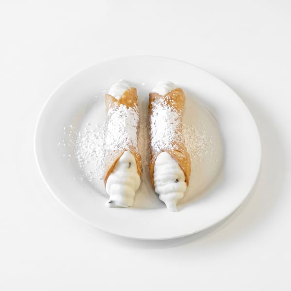 Two cannolis with powdered sugar and cream filling on a white plate.