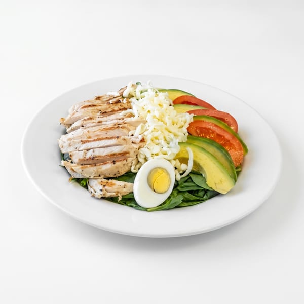 Grilled chicken salad with spinach, avocado, tomatoes, shredded cheese, and a hard-boiled egg.
